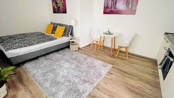 A bedroom with a bed, bedside table, lamp, and a small table with chairs.