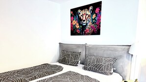 A bedroom with two beds, a grey headboard, a wall-mounted painting of a leopard, and a small round table with a remote control.