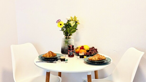 A dining table with two white chairs, a vase with flowers, and a fruit plate.