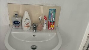 Un lavabo de salle de bain avec des articles de toilette, notamment un savon Dove, un tube de dentifrice Colgate et un flacon de savon pour les mains Carex.