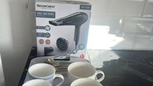 Un comptoir de cuisine avec un étui pour sèche-cheveux, un sèche-cheveux et quatre tasses blanches disposées sur un plateau.