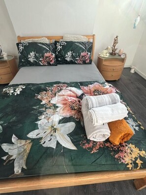 A neatly made bed with floral bedding, two pillows, and a bedside table with a lamp and a small figurine. - Oak Tree Lane Apartment in Birmingham (Birmingham)