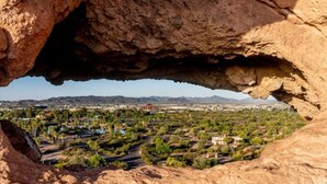 Formação rochosa natural com vista para uma paisagem urbana e vegetação.