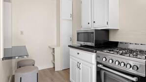 Cozinha compacta com armários brancos, fogão a gás, micro-ondas e dois bancos.