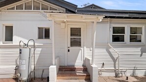 Uma casa branca com porta da frente, aquecedor de água e varanda coberta.