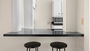 Uma cozinha moderna com bancada preta, dois bancos e armários brancos.