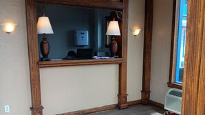 A reception area with wooden beams, a reception desk, two wall-mounted lamps, a first aid kit, and a window with a view of the outside. - Ball Parks Inn (Branson)