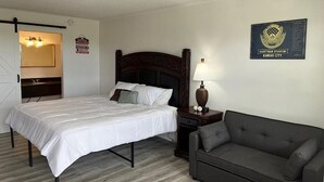 A hotel room with a bed, a nightstand, a lamp, a couch, and a wall plaque. - Ball Parks Inn (Branson)