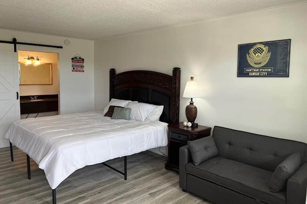 A hotel room with a bed, a nightstand, a lamp, a couch, and a wall plaque.