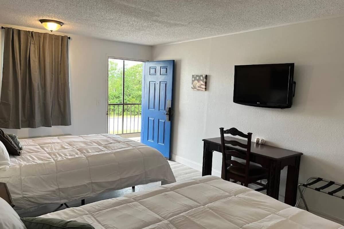 A hotel room with two beds, a TV, a desk, and a window with curtains.