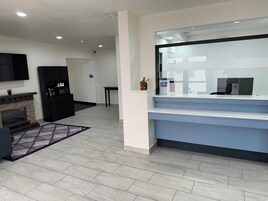 Uma área de recepção moderna com divisória de vidro, uma TV de tela plana na parede, uma lareira de pedra e uma pequena mesa com uma planta.
