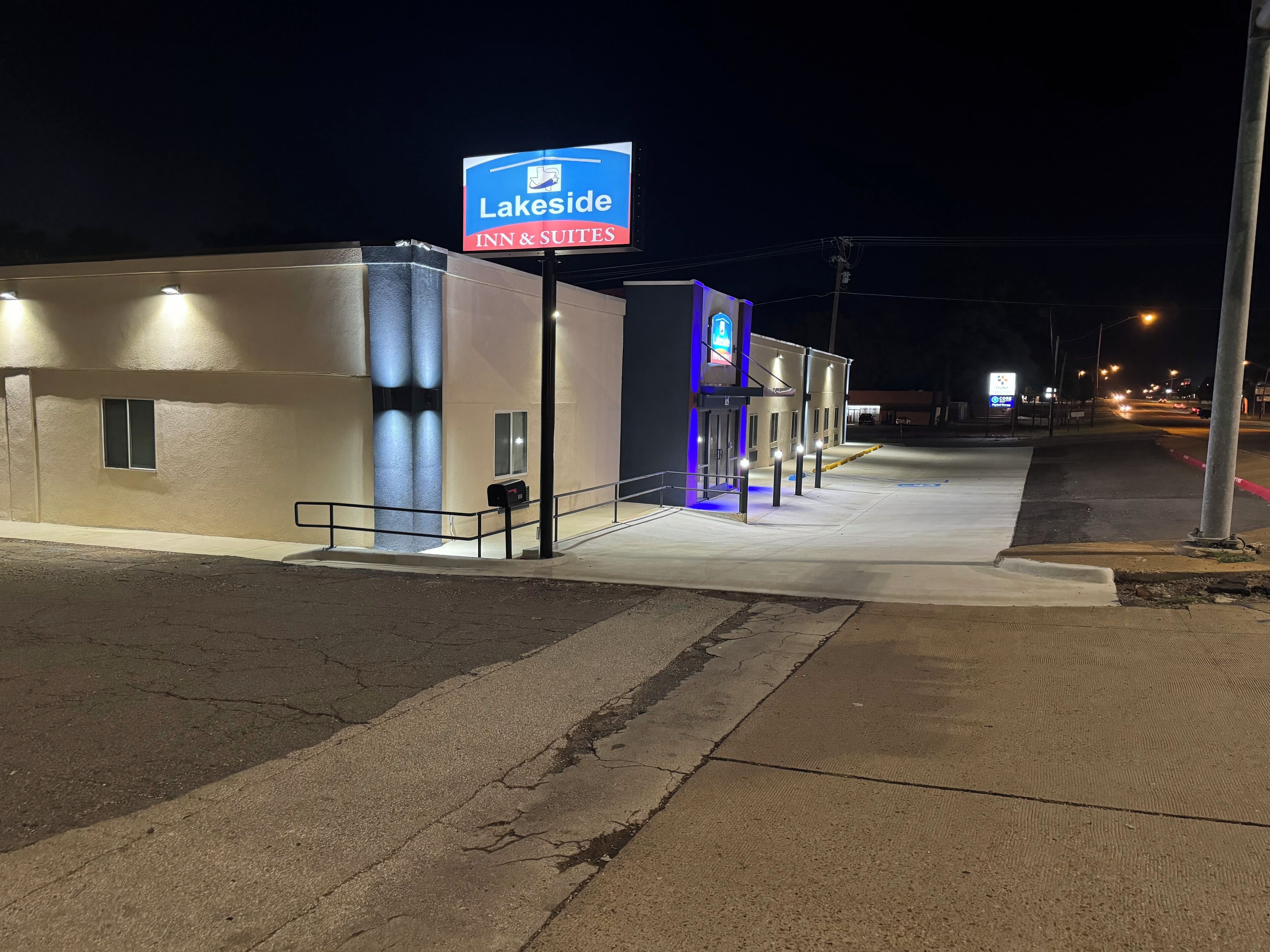 A Lakeside Inn & Suites building at night with illuminated signage, a parking lot, and a sidewalk leading to the entrance.