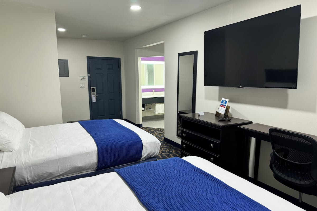 A hotel room with two beds, a desk, a TV, and a mirror.