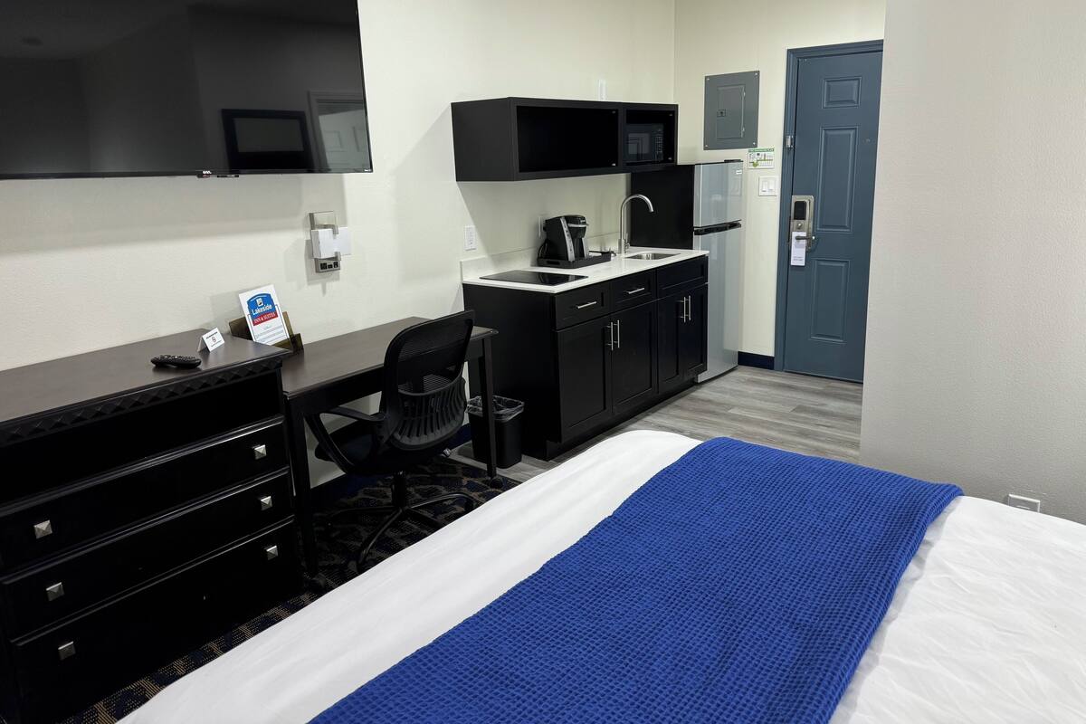 A hotel room with a bed, a desk, a chair, a microwave, a coffee maker, and a door.