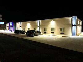 Um edifício com um estacionamento e dois carros estacionados em frente.