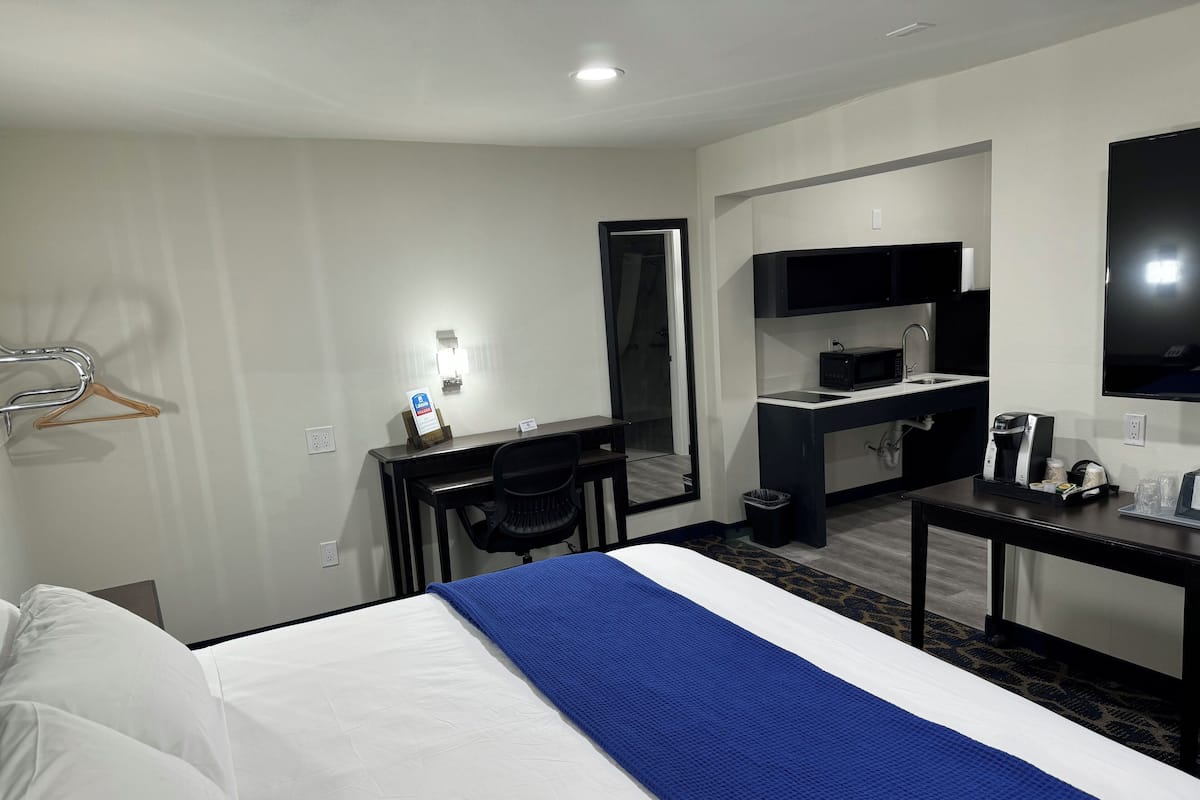 A hotel room with a bed, a desk, a chair, a microwave, a coffee maker, and a TV.