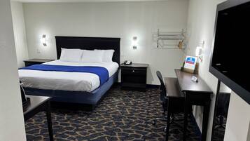 A hotel room with a bed, a desk, a chair, a TV, and a small table.