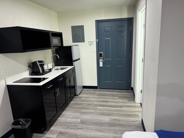 A compact kitchen with black cabinets, a stainless steel sink, and a coffee maker. - Lakeside Inn & Suites (Lone Star)