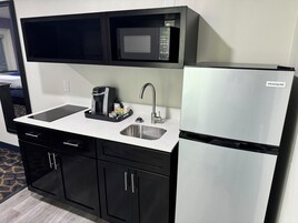 Uma cozinha compacta com micro-ondas, cafeteira, pia e geladeira.