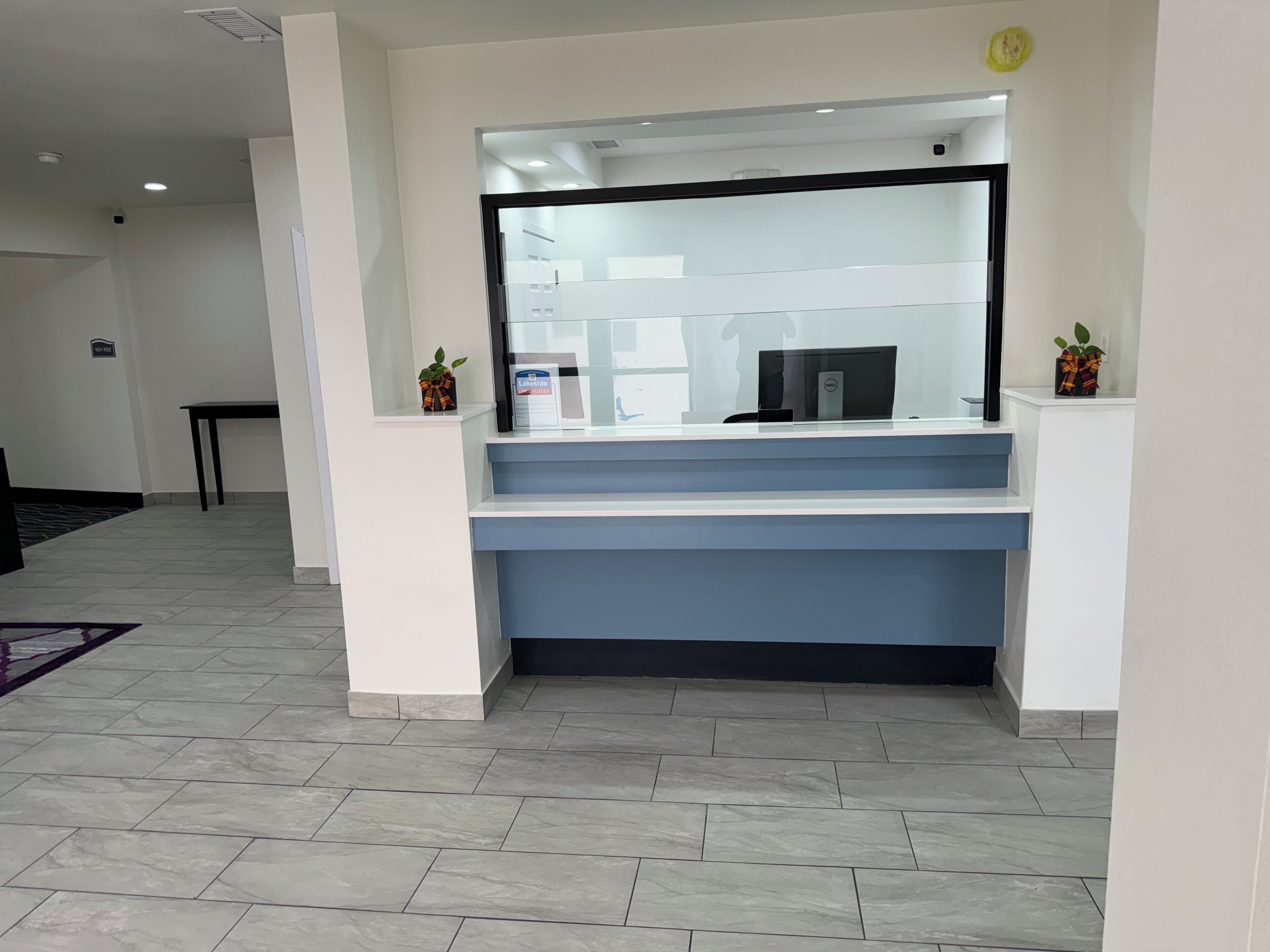 A reception area with a glass partition, a Dell computer, and a small plant on the counter.