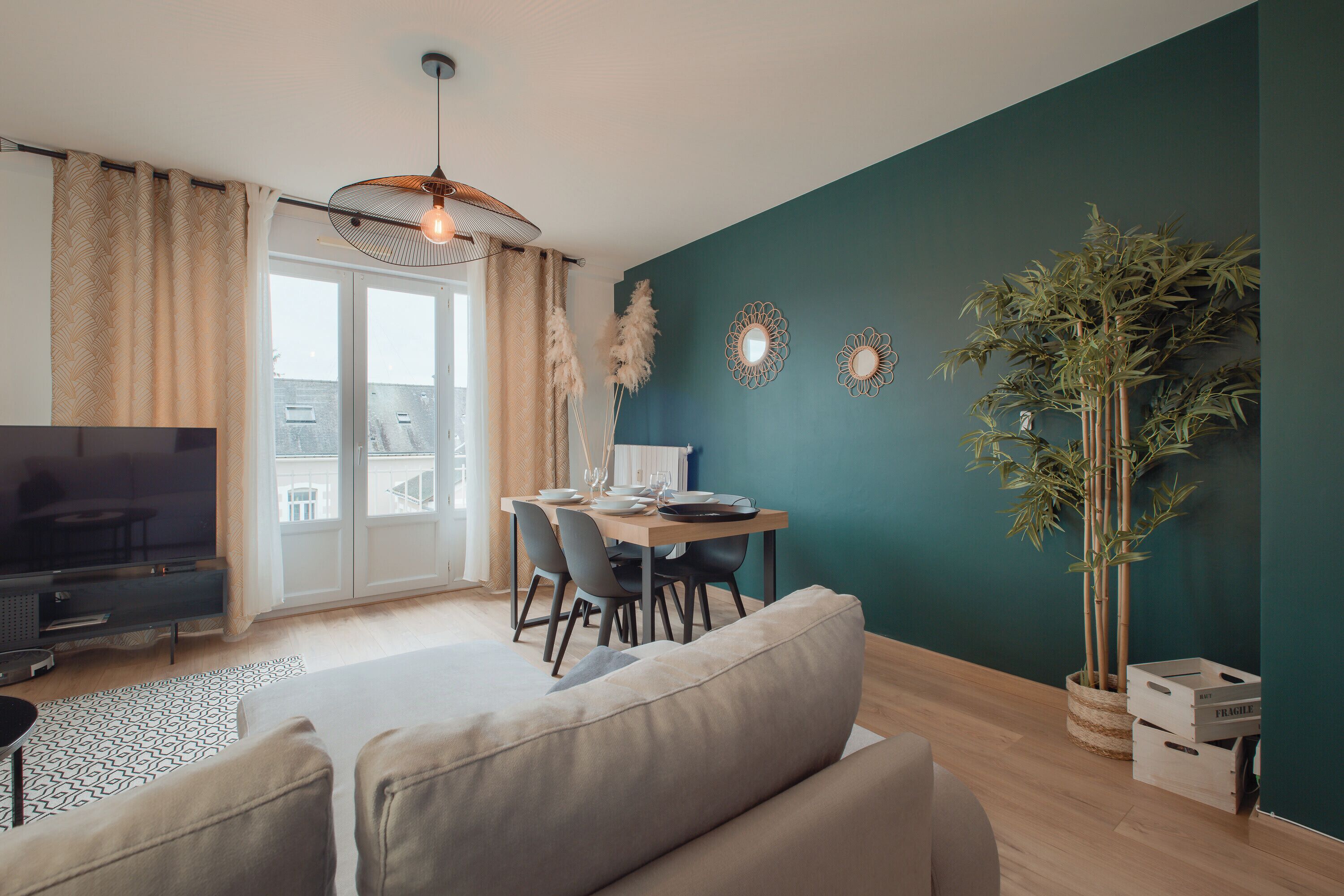 Ein modernes Wohnzimmer mit einer Couch, einem Esstisch und Stühlen. Es gibt einen Fernseher, eine Pflanze und dekorative Spiegel an der Wand.