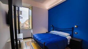 Une chambre à coucher comprenant un lit, une table de chevet, un bureau et une fenêtre donnant sur des immeubles.