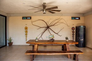 Un comedor con mesa de madera y bancos, ventilador de techo, decoración en la pared y refrigerador.