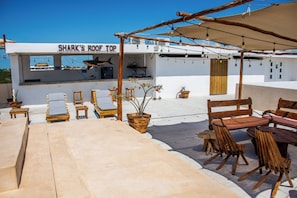 Um bar no terraço chamado 'Shark's Roof Top', com área externa para sentar, um piano e vista da cidade.