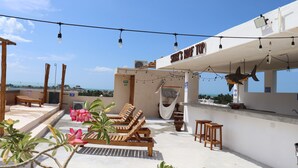 A rooftop terrace with wooden lounge chairs, a hammock, and string lights. - LaFamilia Casa and Suites (Isla Holbox)