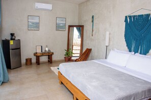 Un dormitorio con cama, escritorio, refrigerador, planta en maceta y espejo.
