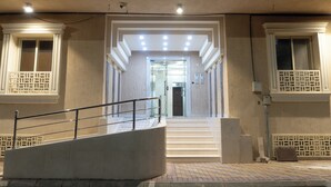 Entrada de un hotel con una escalera central, un vestíbulo cubierto y una cámara de seguridad.