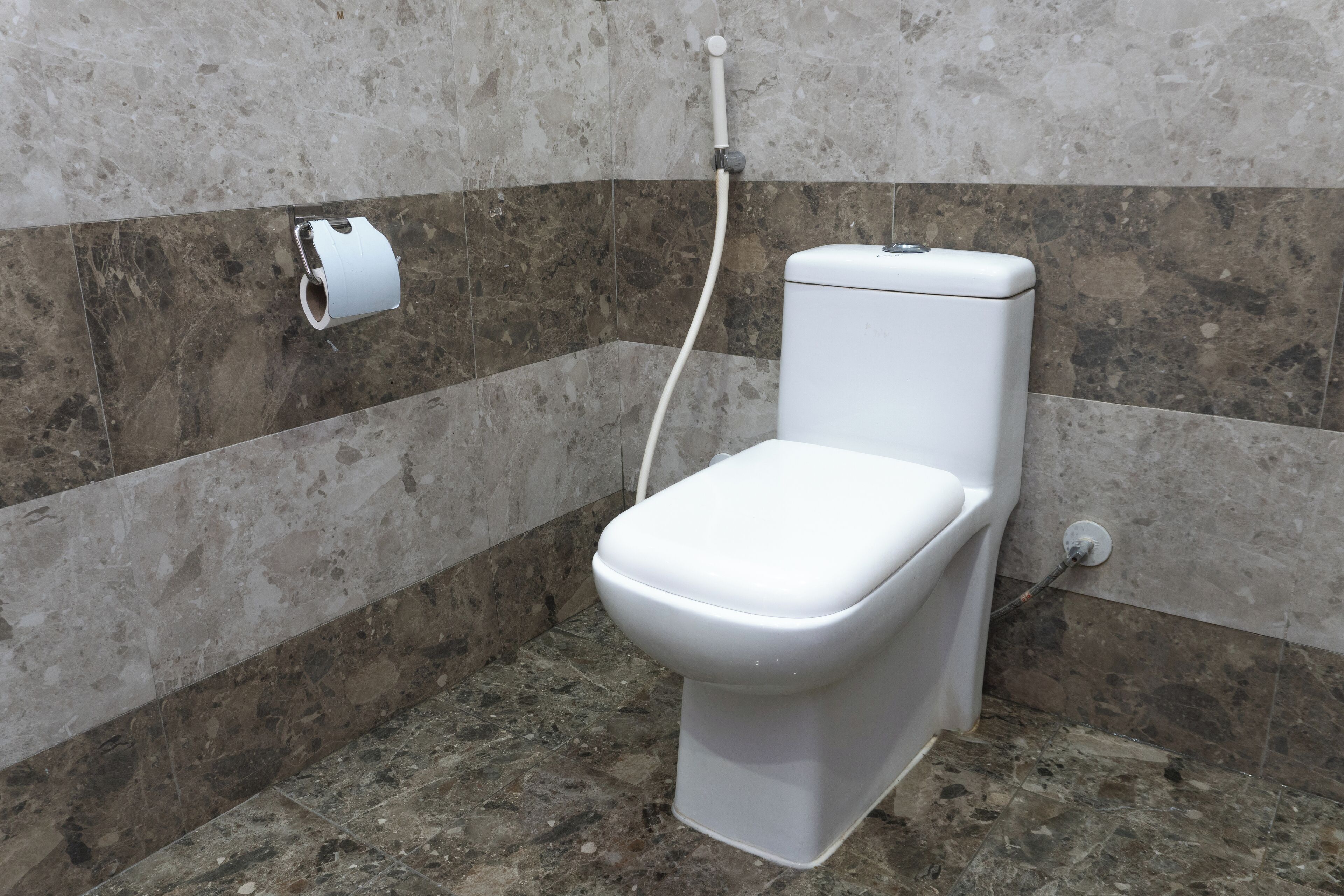 Un baño moderno con inodoro, dispensador de toallas de papel y cabezal de ducha.