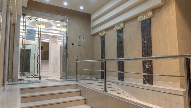 Un moderno vestíbulo de hotel con una escalera de mármol, un acceso por puerta de cristal y un letrero con texto.