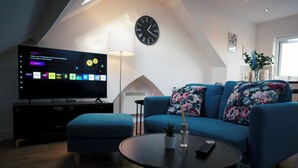 Ett modernt vardagsrum med en platt-TV, en blå soffa, ett soffbord och en klocka på väggen.