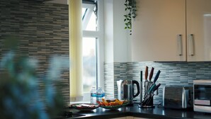 Ett kök med modern design, med kakel som stänkskydd, ett fönster med persienner och olika köksmaskiner.