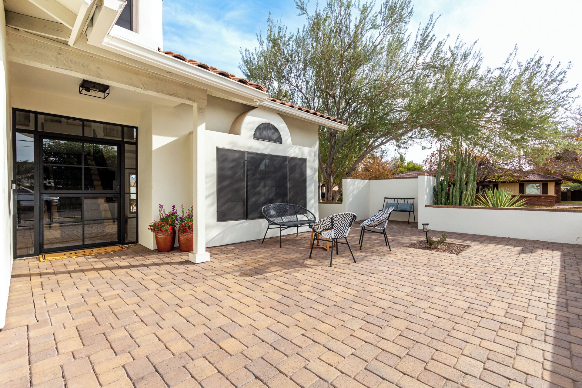 A patio area with a brick floor, two black chairs, and a bench.
