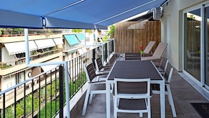 En balkon med et bord og stole, et træhegn og udsigt til nabobygninger.