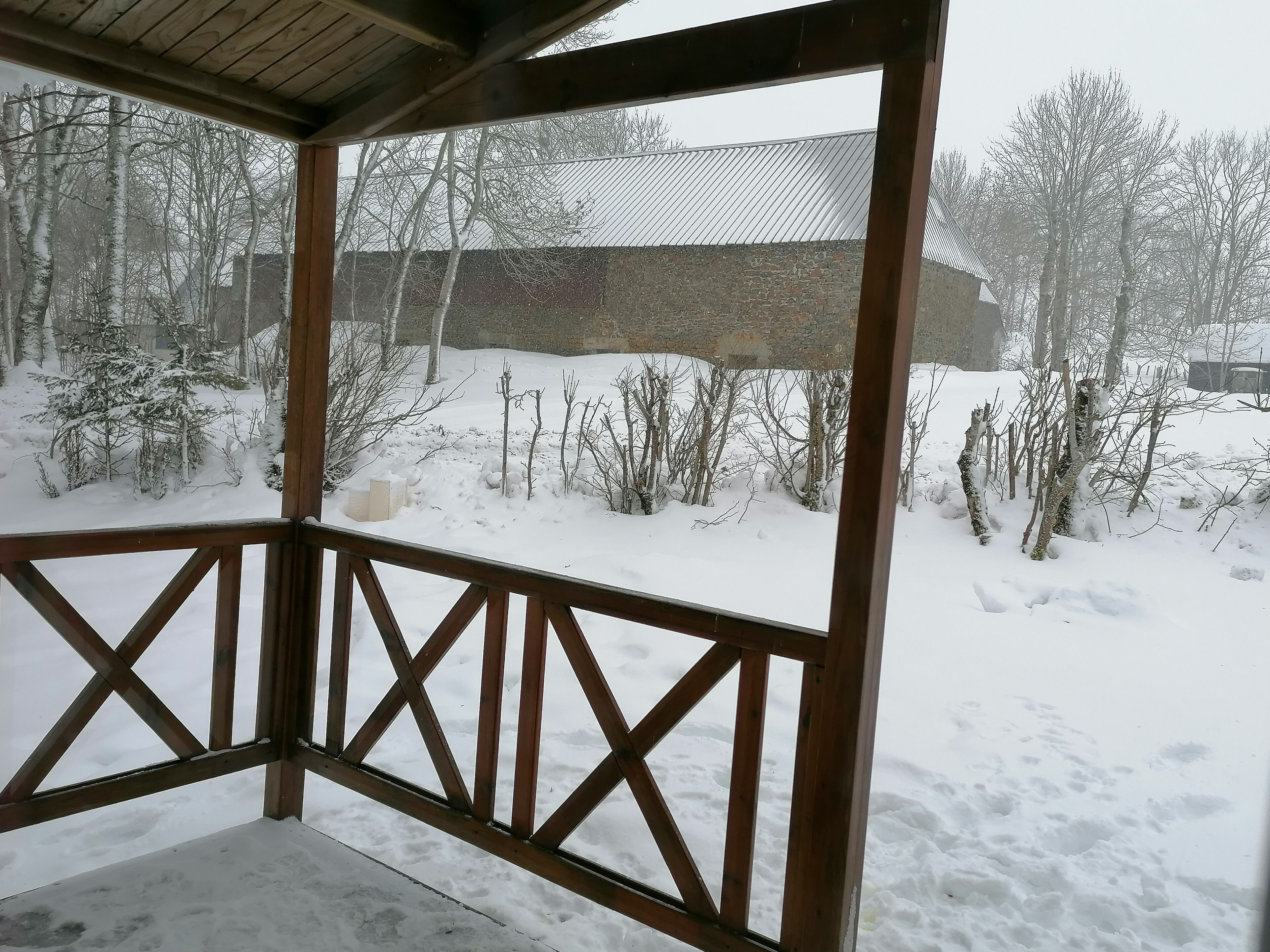 Un espacio al aire libre cubierto con barandilla de madera, suelo cubierto de nieve y árboles sin hojas.