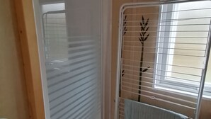 Een kamer met een witte radiator, een raam met zonwering en een metalen rek met een handdoek.