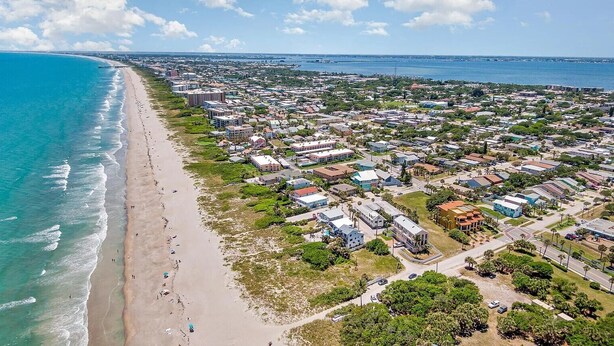 Vista aérea de un pueblo costero con playa, edificios residenciales y un puerto deportivo.