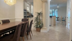 Un comedor con una mesa y sillas de madera, una araña, una planta en maceta y vistas de la cocina y el salón.