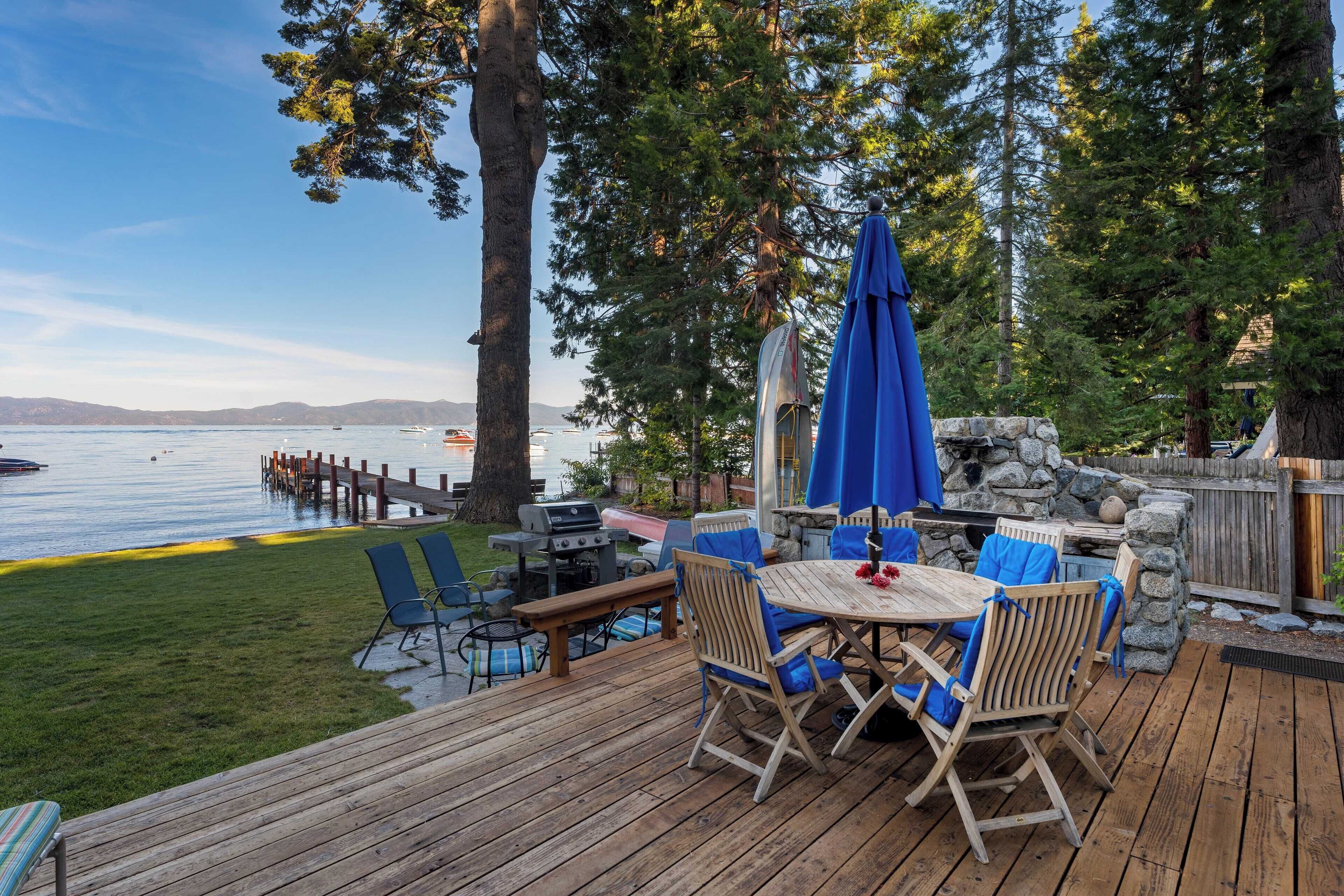 A wooden deck with a table and chairs, overlooking a lake with boats and a dock.