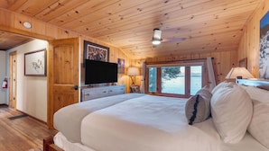 A wooden cabin bedroom with a bed, a television, a window with a view of a lake, and a ceiling fan. - Lakefront Haven by Avantstay Minutes to Ski Resorts Private Dock (Homewood)