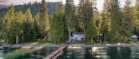 Una propiedad junto al lago con un muelle, rodeada de árboles altos y una casa con terraza.