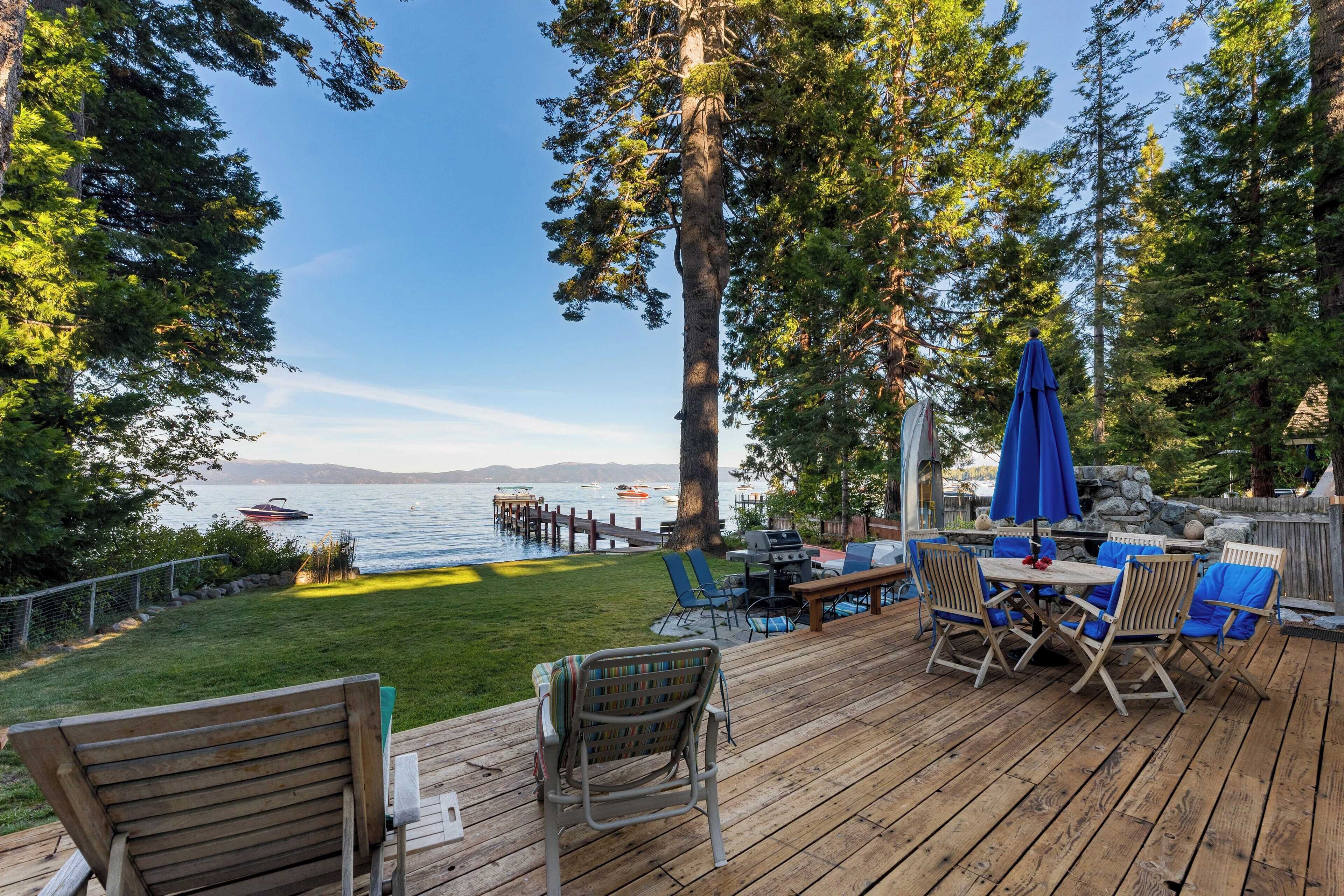 A wooden deck with outdoor furniture, a grill, and a view of a lake with boats.