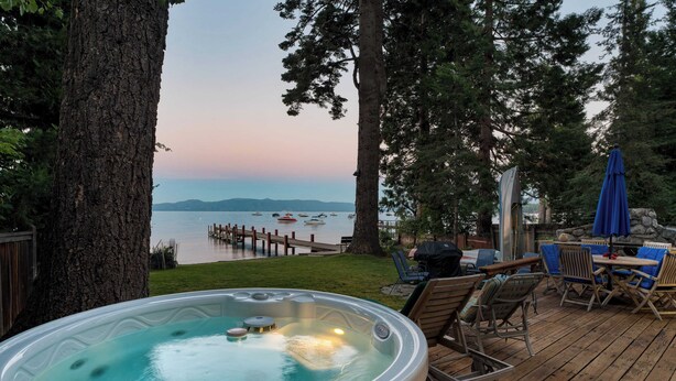 A hot tub on a wooden deck with a view of a lake and dock. - Lakefront Haven by Avantstay Minutes to Ski Resorts Private Dock (Homewood)