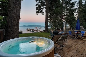 Een hottub op een houten terras met uitzicht op een meer en een steiger.