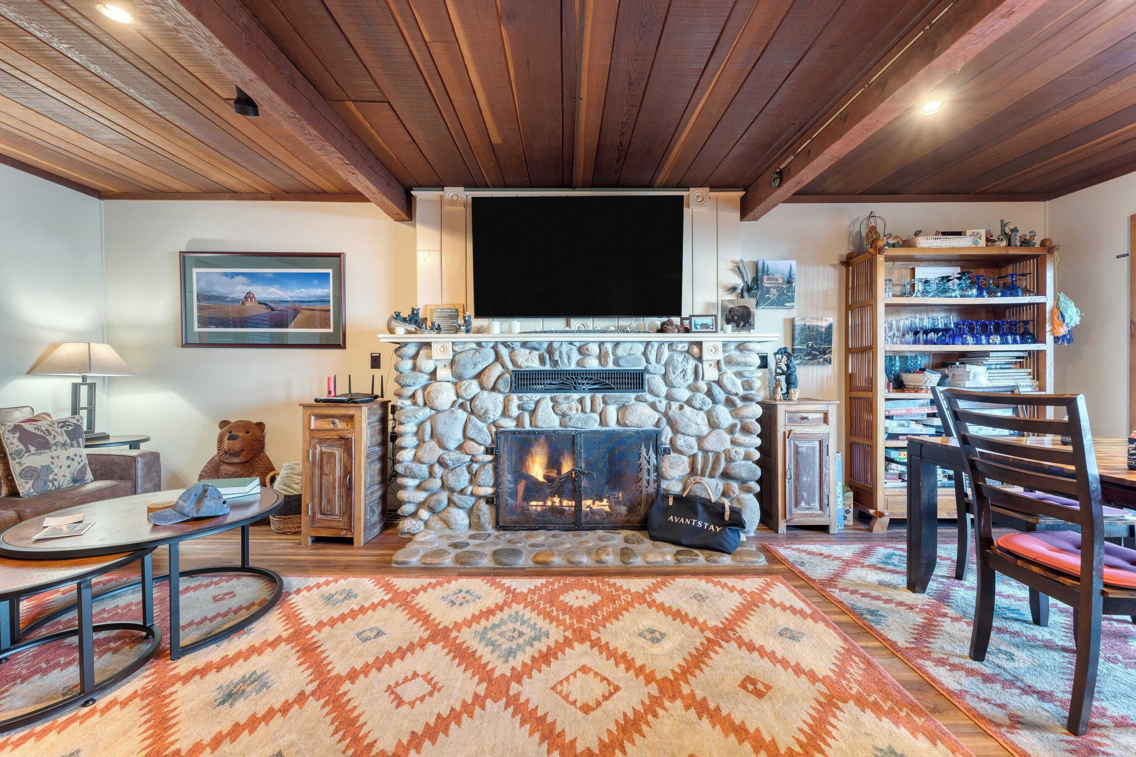 A cozy living room with a stone fireplace, a television mounted above it, and a bookshelf filled with decorative items.