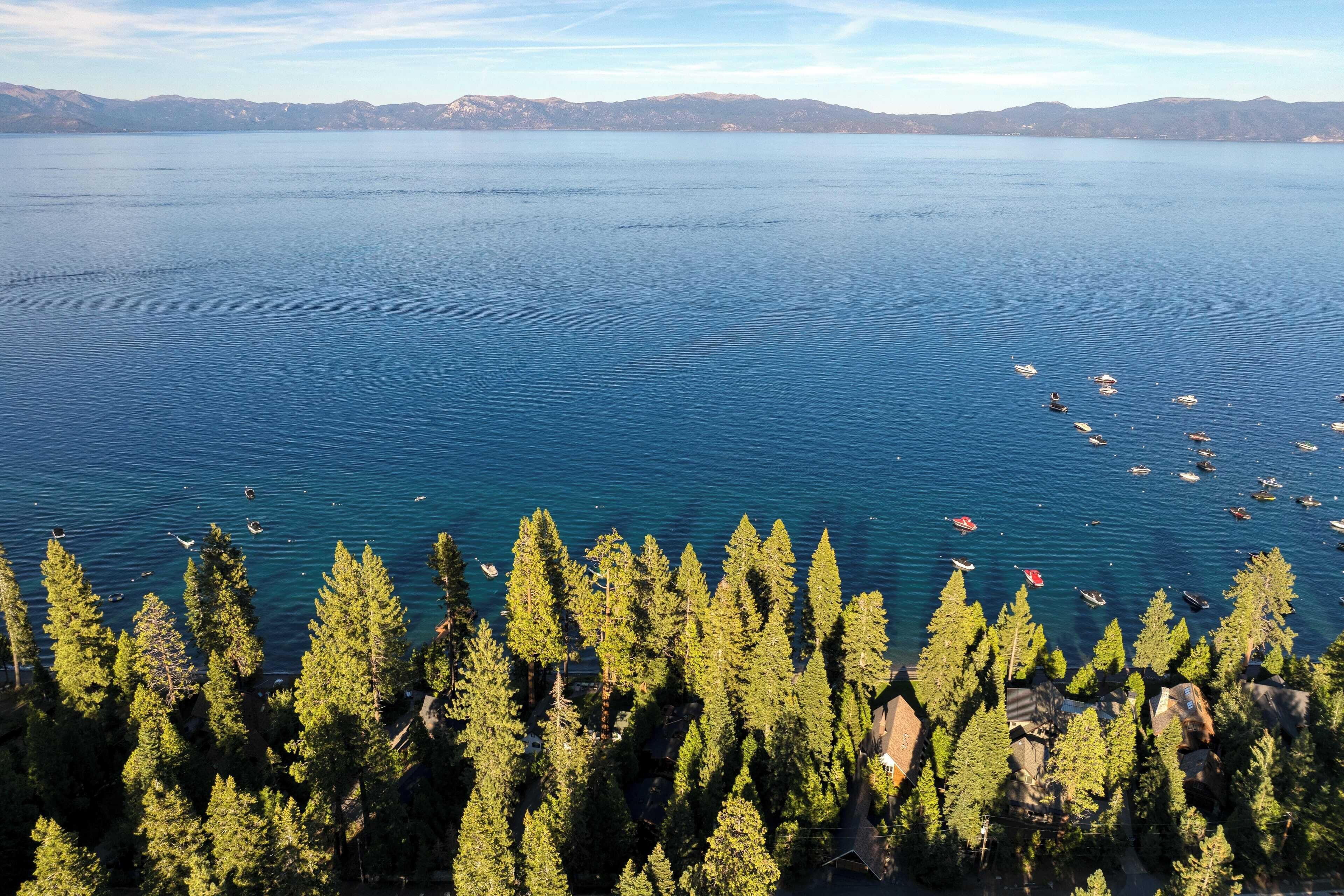 A lake with boats, surrounded by dense forest and distant mountains.