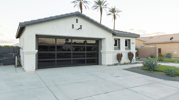 Une maison moderne de plain-pied, dotée d  ’un grand garage, d’un petit porche et d’un jardin bien entretenu où l’on trouve des cactus et des arbustes.